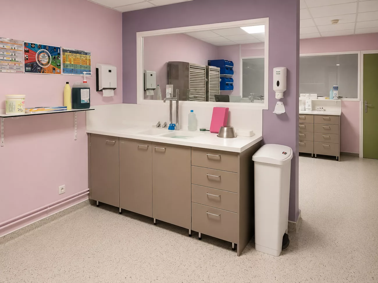 Salle de soins bébé de la maternité du Centre Hospitalier de l'Ouest Vosgien : paillasse avec vasque intégrée, façades taupe, grand miroir mural, distributeurs de savon et d'essuie-mains.